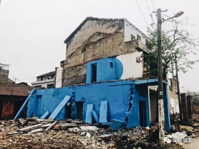 △ 這棟建筑是臨江最近的半拆遷建筑物的遺留，沅江和堤壩成為了展覽的天然背景。創(chuàng)作團(tuán)隊(duì)對這棟建筑進(jìn)行了半涂裝，將符號(hào)性的沅水曲線與拆遷進(jìn)行中的建筑立面進(jìn)行意義的疊造，它們共同觸發(fā)了場所空間多元語境的生成，把拆遷這種暫時(shí)破壞性、干擾性的介入行動(dòng)與沅水右岸發(fā)展的未來性、美好性緊密融合。